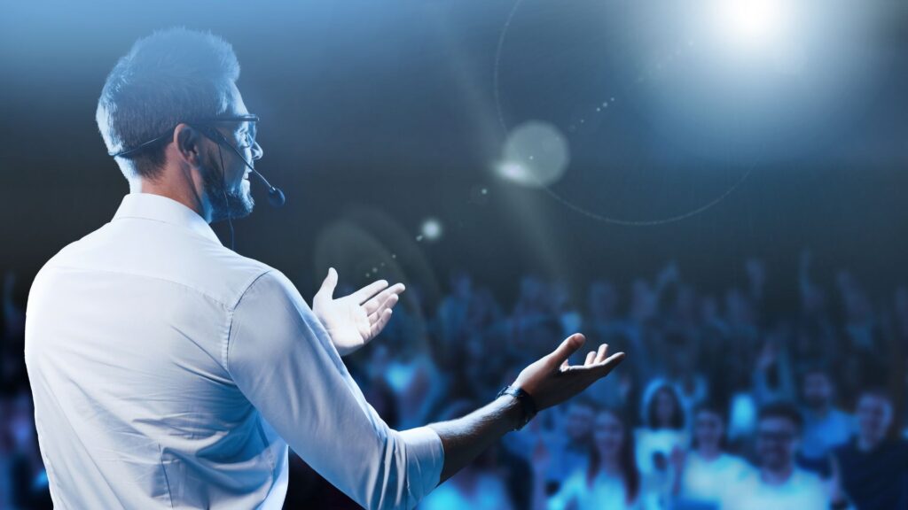 Speaker on stage gesturing to the audience